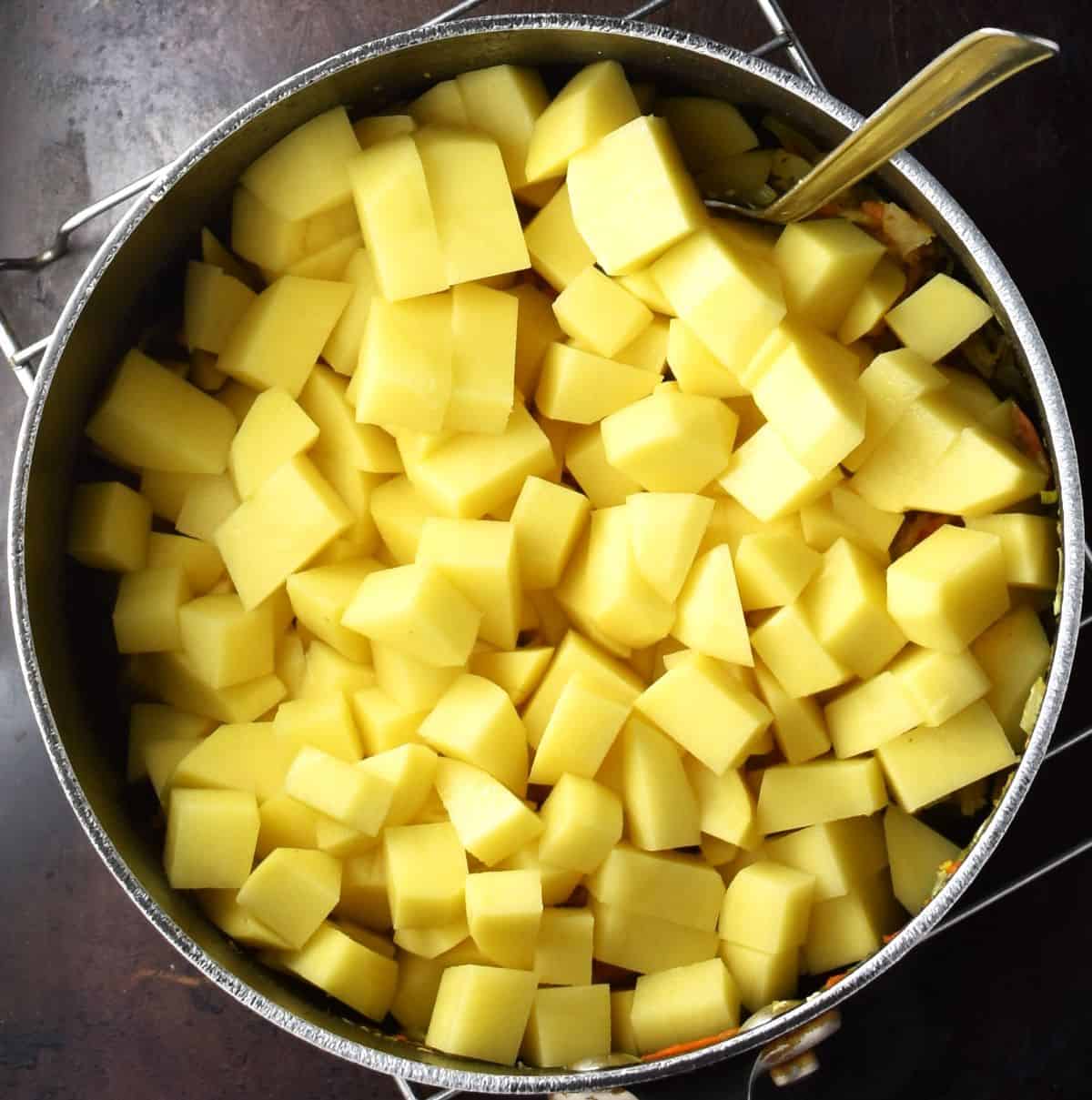 Cubed peeled potatoes in large soup pot with spoon.