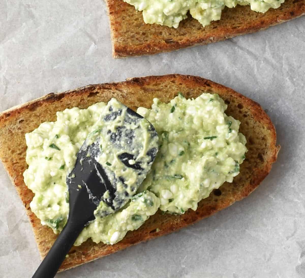 Spreading avocado and cottage cheese mixture on toast with black spatula.