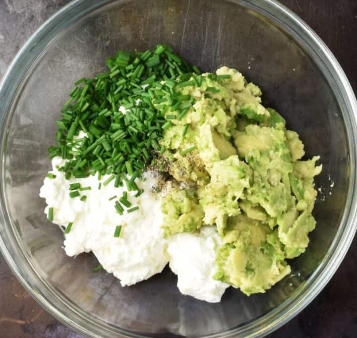 Smashed avocado, cottage cheese and chopped chives in glass bowl.