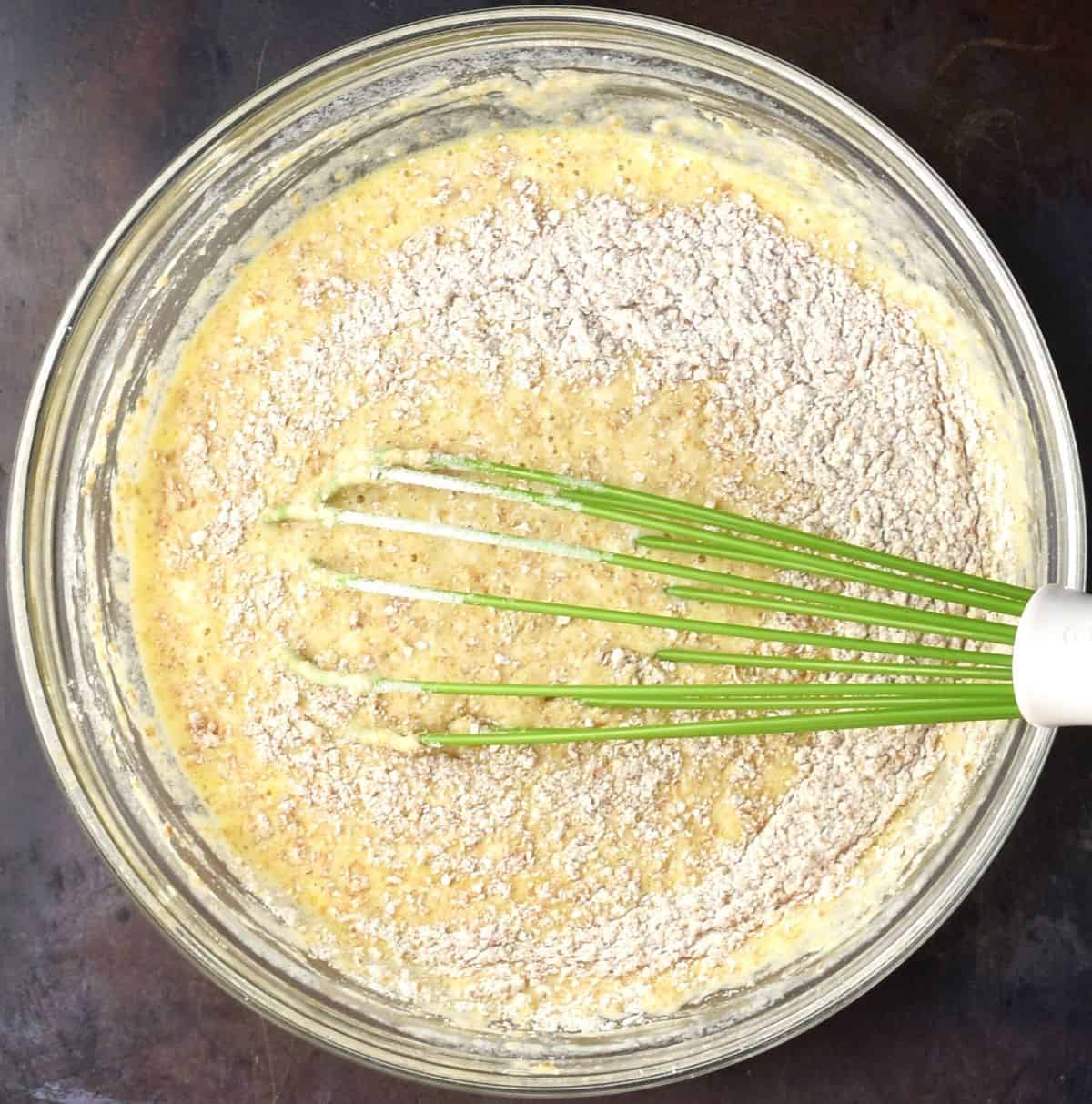 Pancake batter with flour visible on top in mixing bowl with green whisk.