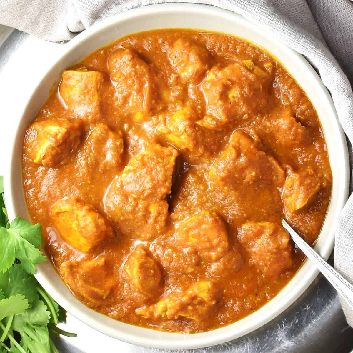 Top down view of chicken pumpkin curry in grey bowl with spoon.