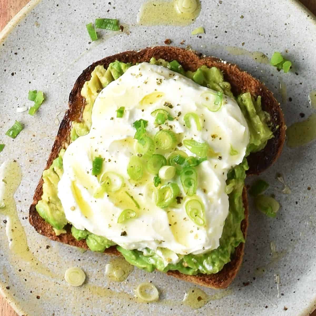 Top down view of avocado toast with whipped feta, scallions and honey on speckled plate.
