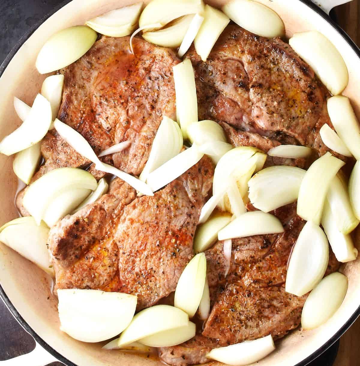 4 pork shoulder steaks with sliced onions in large pan.