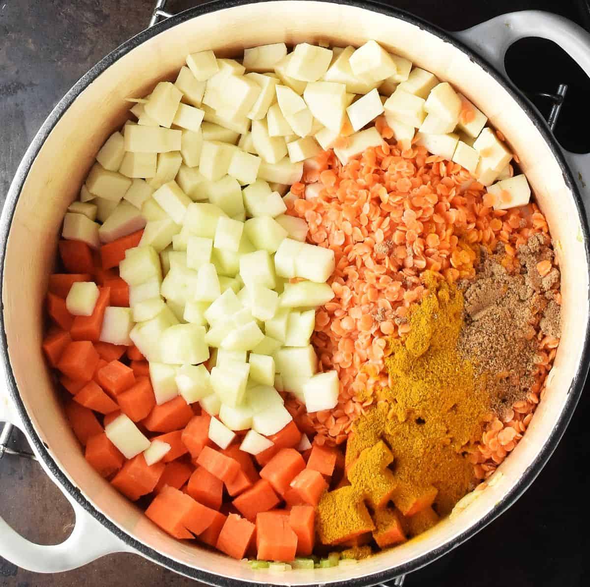 Cubed vegetables, red lentils and spices in large white pot.
