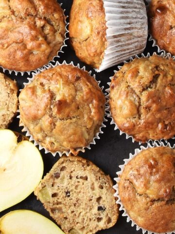 Top down view of pear muffins in white paper cases and halved pear.