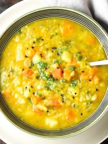 Close-up top down view of vegetable mulligatawny soup in green bowl with spoon on white plate.