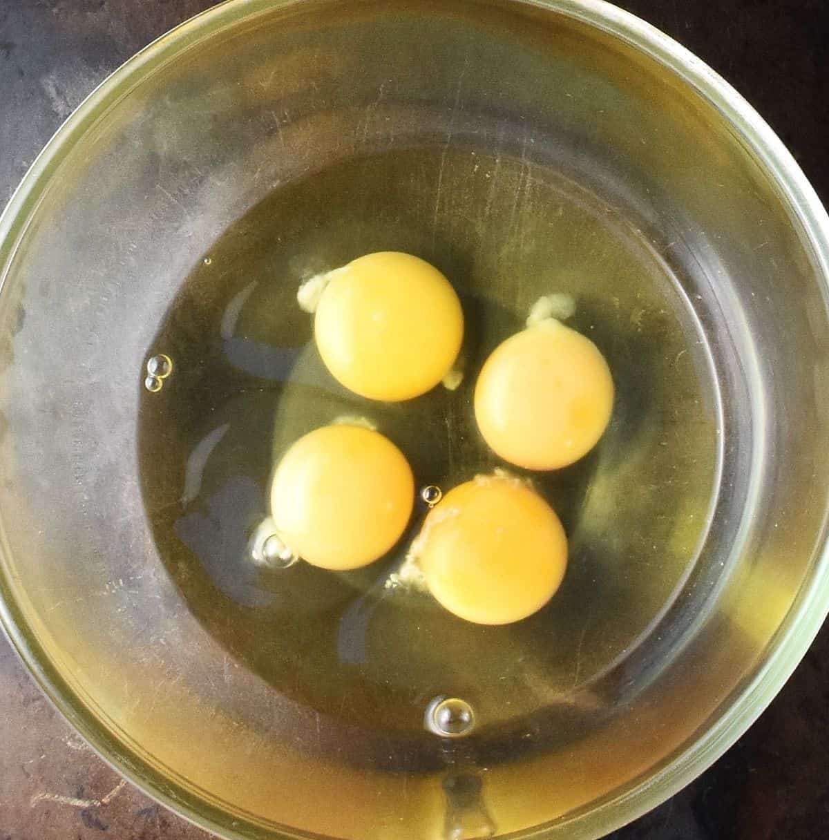 4 raw eggs in large glass bowl.