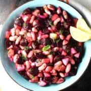 Top down view of pickled beet salad with beans and vegetables in blue bowl with lemon wedges.