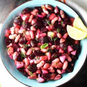 Top down view of pickled beet salad with beans and vegetables in blue bowl with lemon wedges.