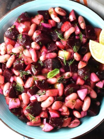 Top down view of pickled beet salad with beans and vegetables in blue bowl with lemon wedges.