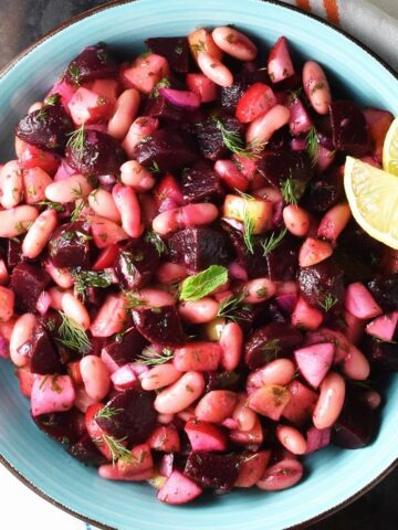 Top down view of pickled beet salad in blue bowl with lemon wedges.