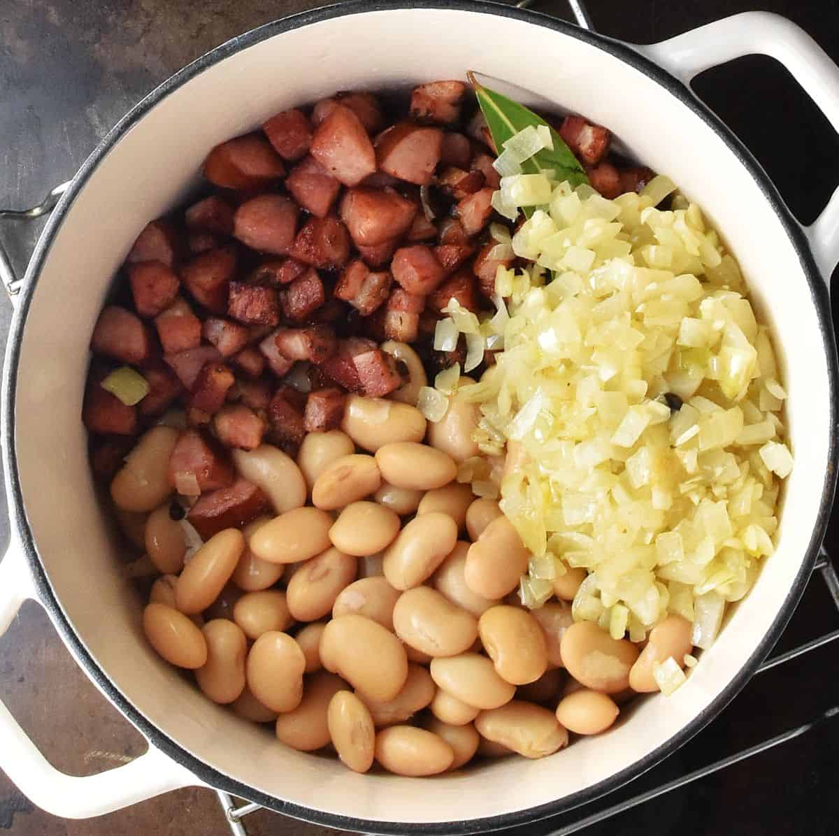 Top down view of butter beans, chopped sausage and onion in white pot.