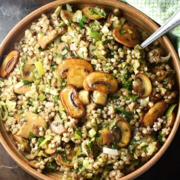 Top down view of cooked buckwheat with browned mushrooms in brown round dish with spoon.