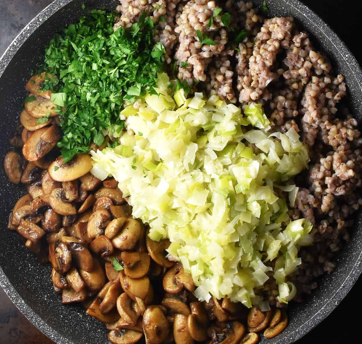 Cooked buckwheat, leek and onion mixture, herbs and sauteed mushrooms in large pan.