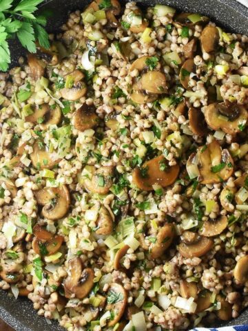 Close-up top down view of buckwheat with mushrooms in large pan with wooden spoon.