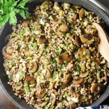 Close-up top down view of buckwheat with mushrooms in large pan with wooden spoon.