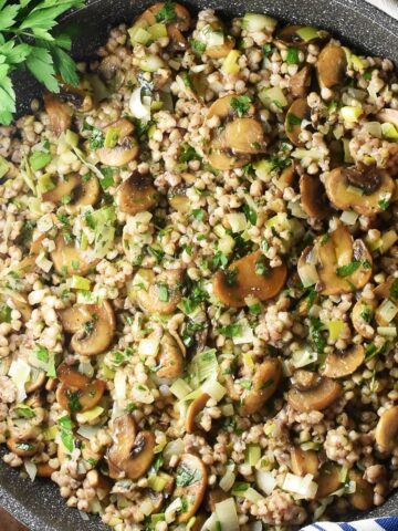 Close-up top down view of buckwheat with mushrooms in large pan with wooden spoon.