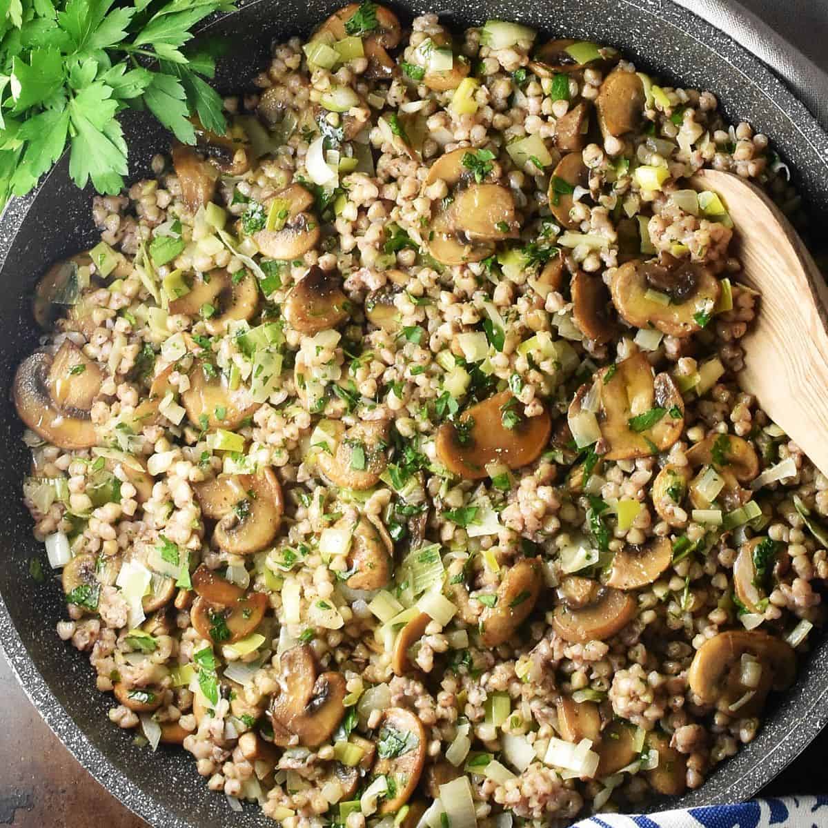 Close-up top down view of buckwheat with mushrooms in large pan with wooden spoon.