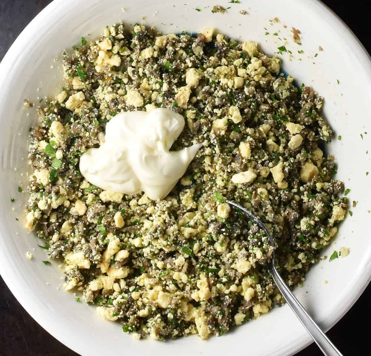 Mushroom and yolk mixture with mayo in large white bowl with spoon.
