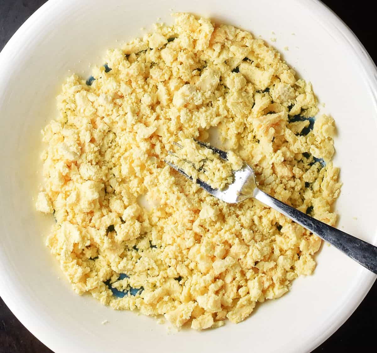 Crumbled egg yolks with fork in white bowl.