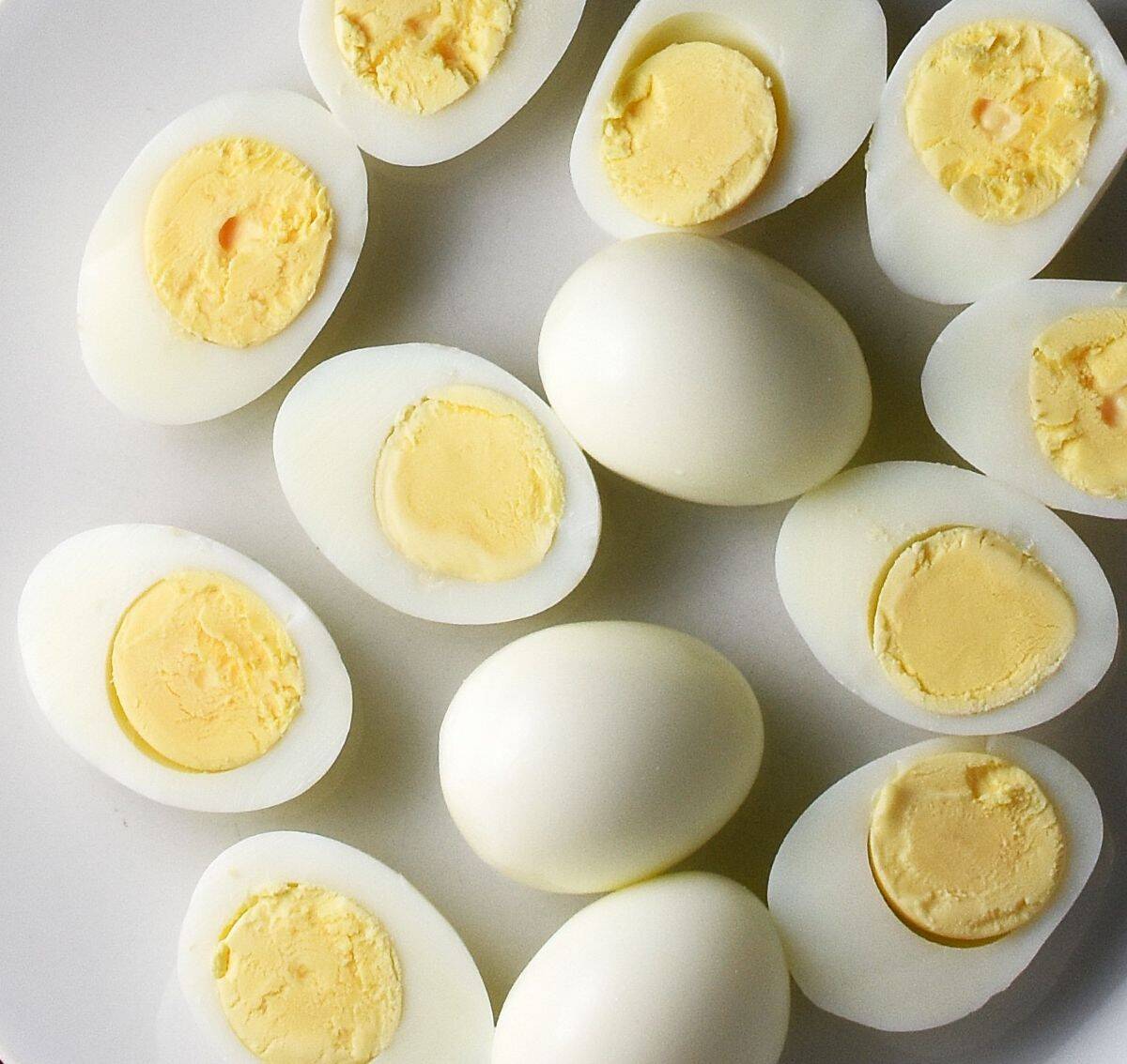 Top down view of halved hard-boiled eggs on white plate.