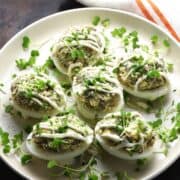 Side view of Polish deviled eggs with herbs on white plate.