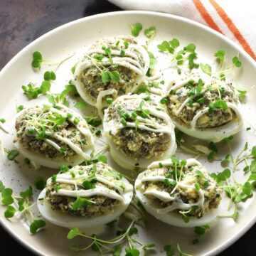 Side view of Polish deviled eggs with herbs on white plate.