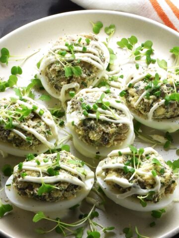 Side view of Polish deviled eggs with herbs on white plate.