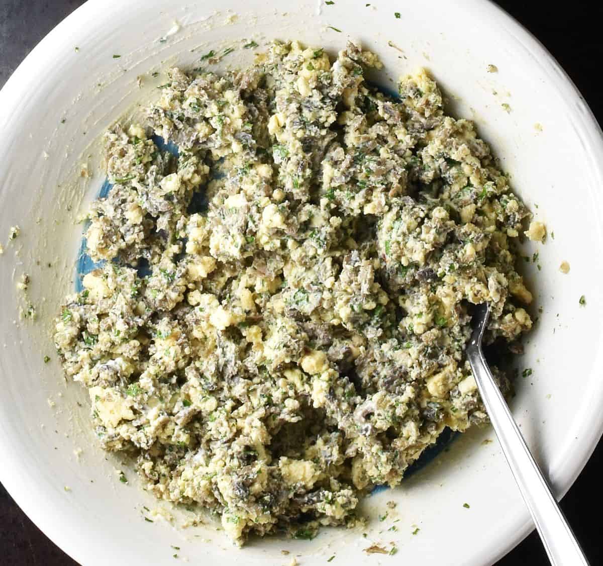 Stuffed egg filling mixture for Polish eggs in white bowl with spoon.