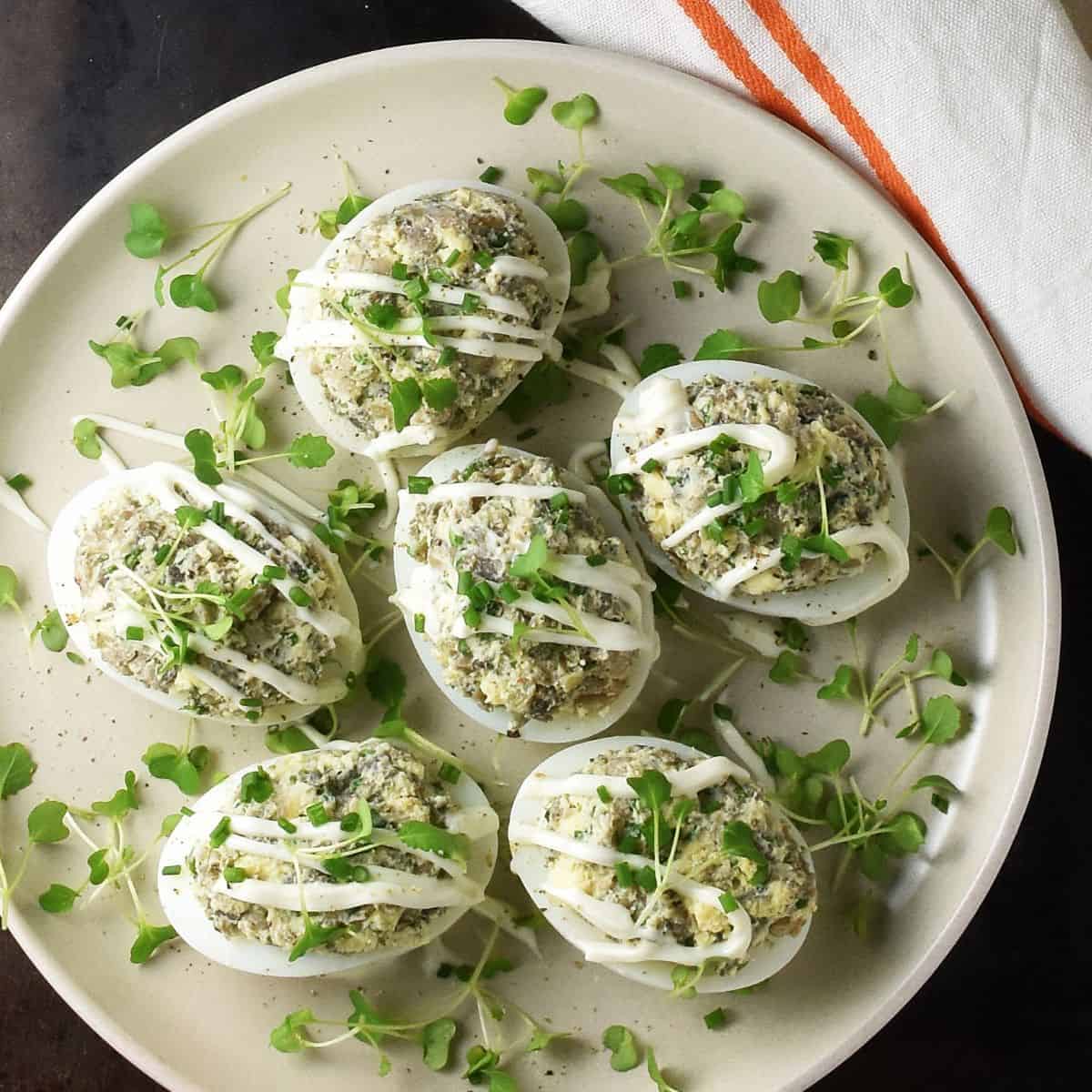 Top down view of Polish deviled eggs with mushrooms topped with herbs and mayo on white plate.