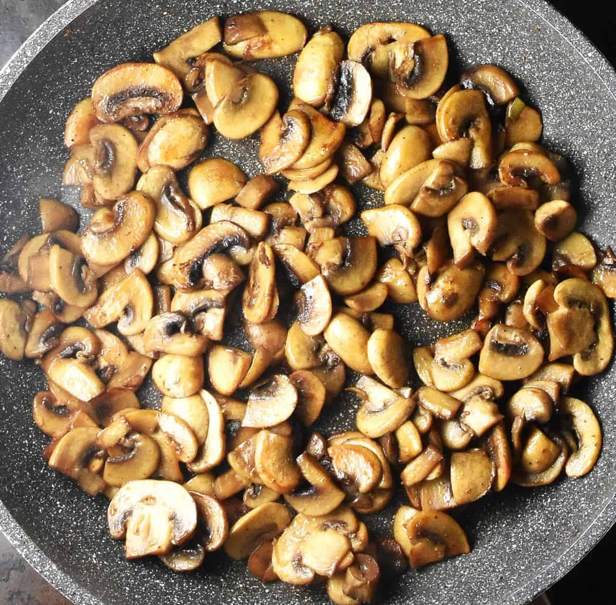 Top down view of browned slices of mushrooms in large pan.