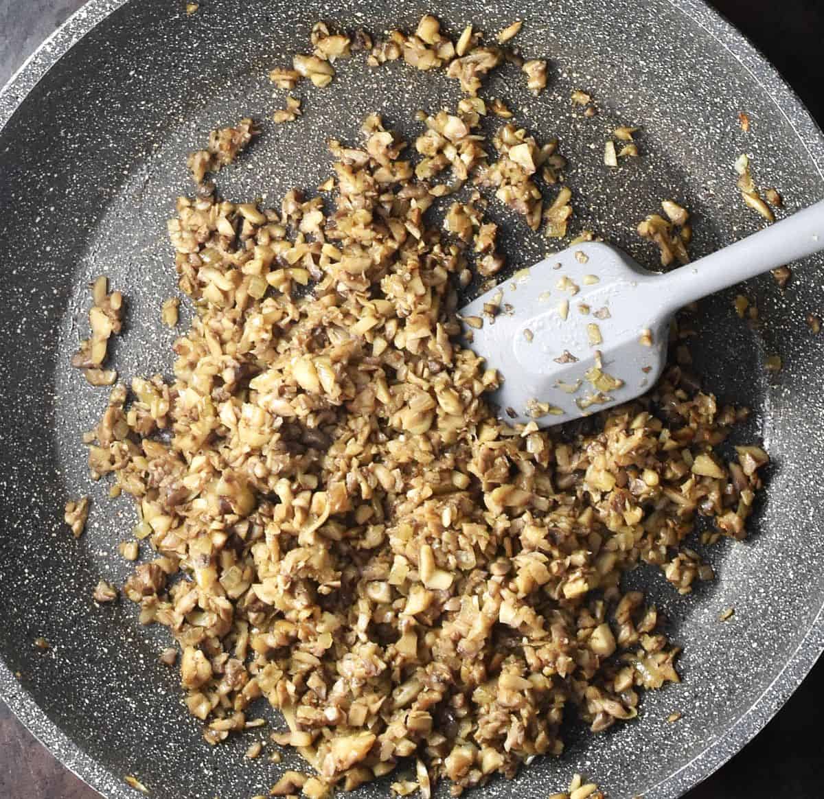 Top down view of sauteed mushroom mixture in large pan with grey spoon.
