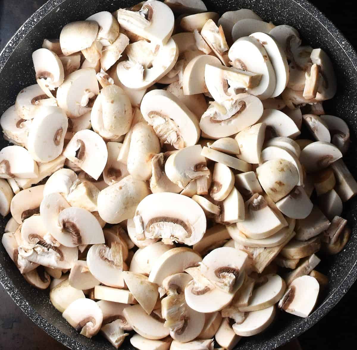 Sliced regular mushrooms in large pan.