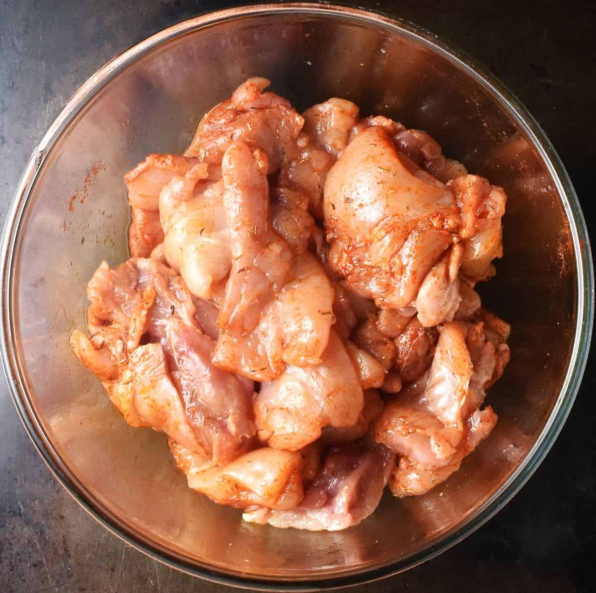 Chicken pieces with spices in glass bowl.