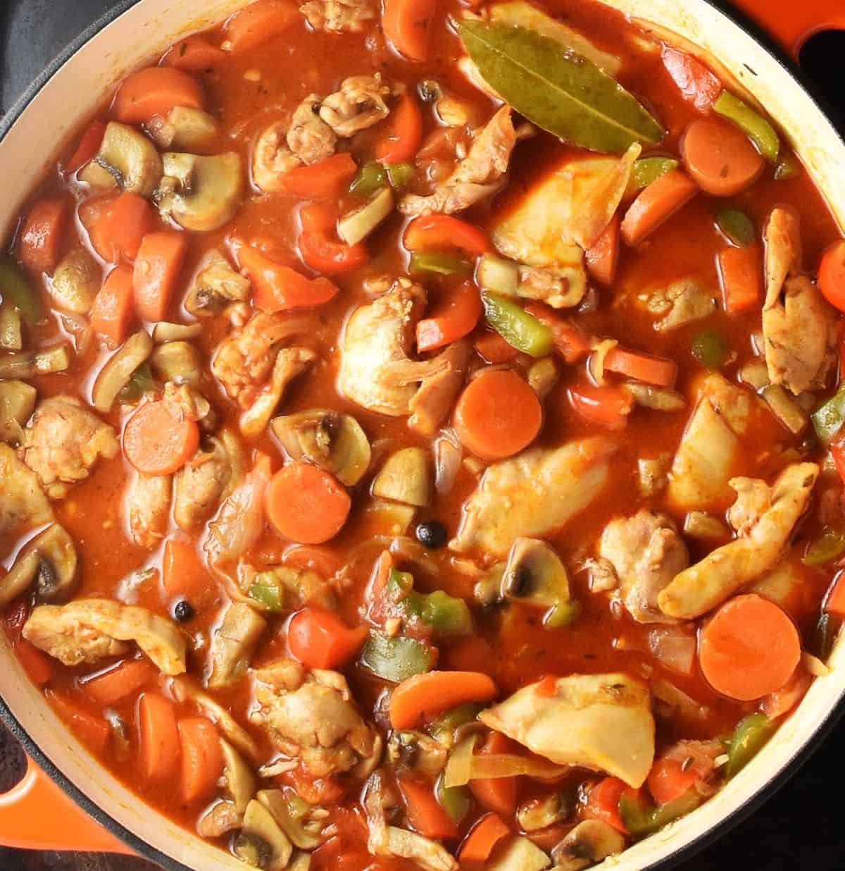 Cooked goulash with chicken and vegetables in large white pan.
