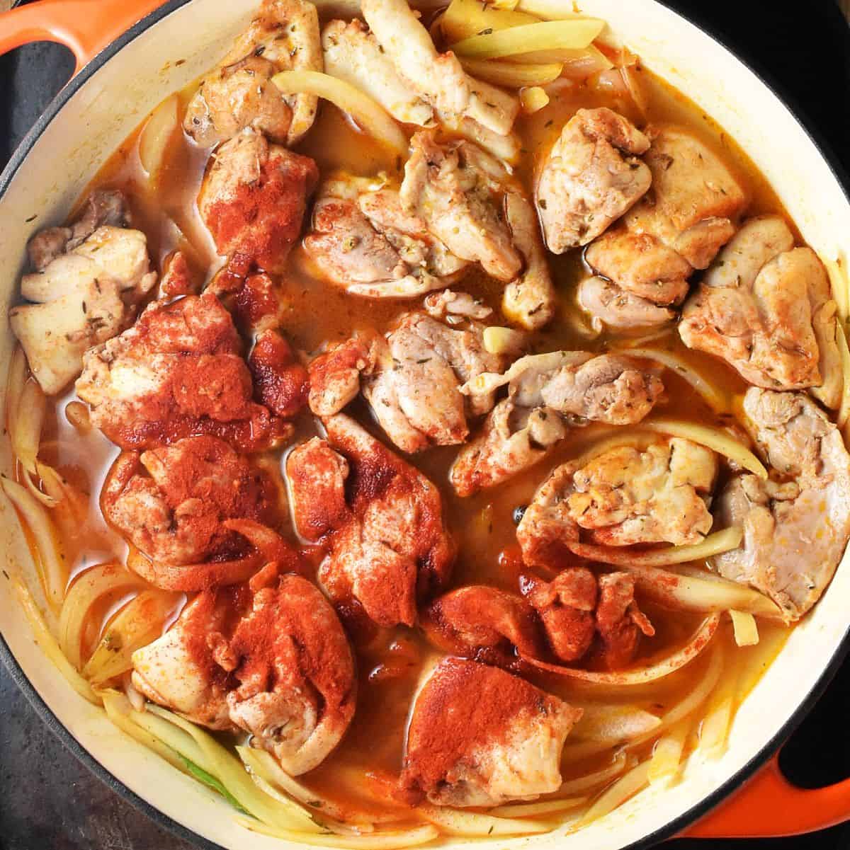 Pieces of chicken with onion and paprika in white pan.