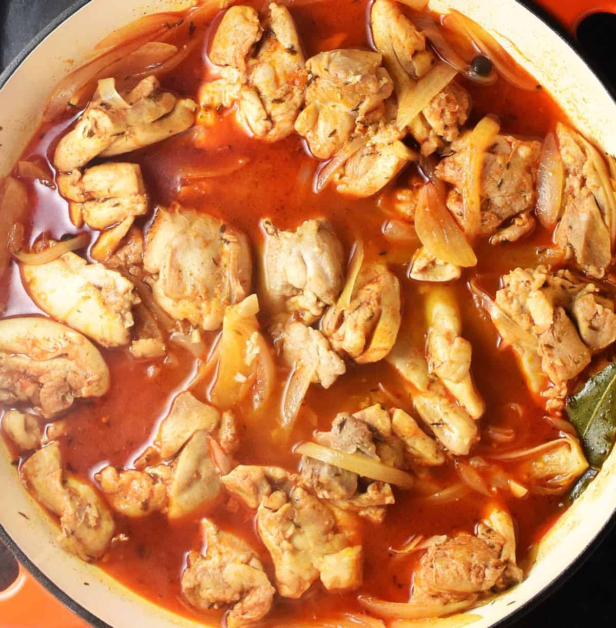 Pieces of chicken in gravy with paprika in large white pan.