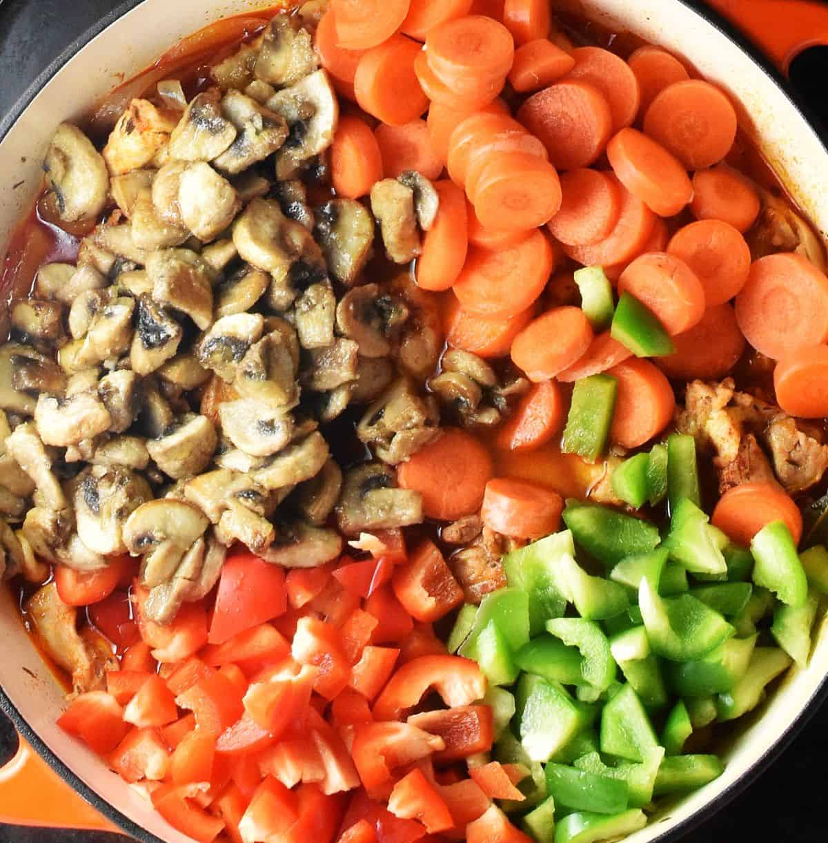Chopped vegetables and mushrooms in large white pan.