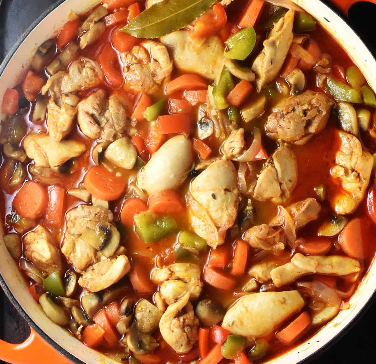 Cooking chicken gulasz with vegetables in white, shallow pan.
