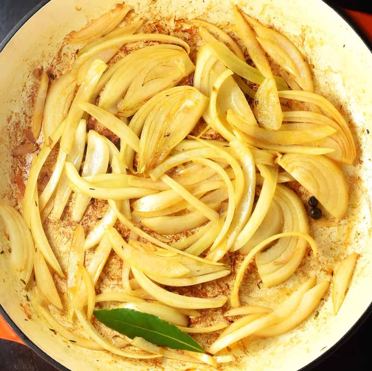Sliced onion and bay leaf in large, shallow pan.