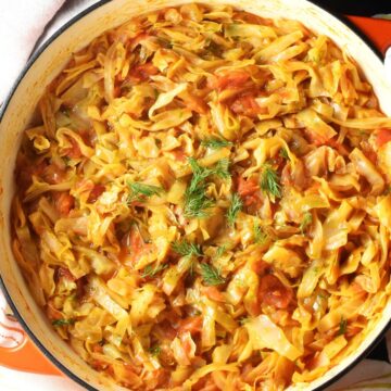 Top down view of stewed cabbage with tomatoes in large white pan.