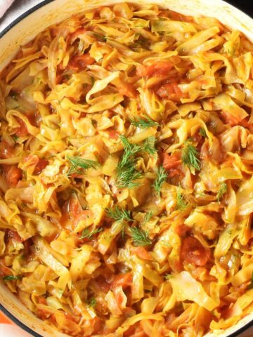 Top down view of stewed cabbage with tomatoes in large white pan.