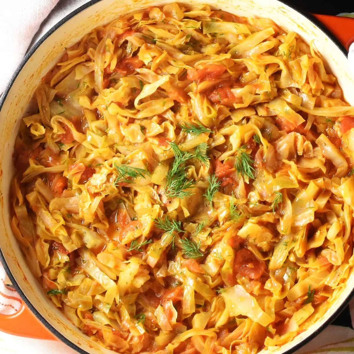 Top down view of stewed cabbage with tomatoes in large white pan.