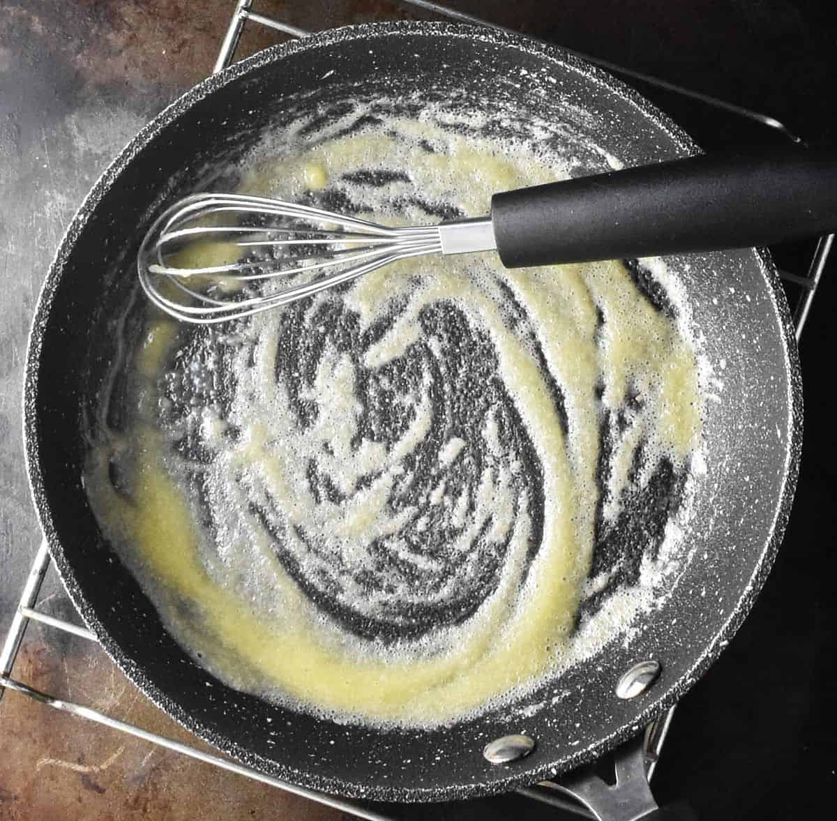 Roux mixture in small black pan with whisk.