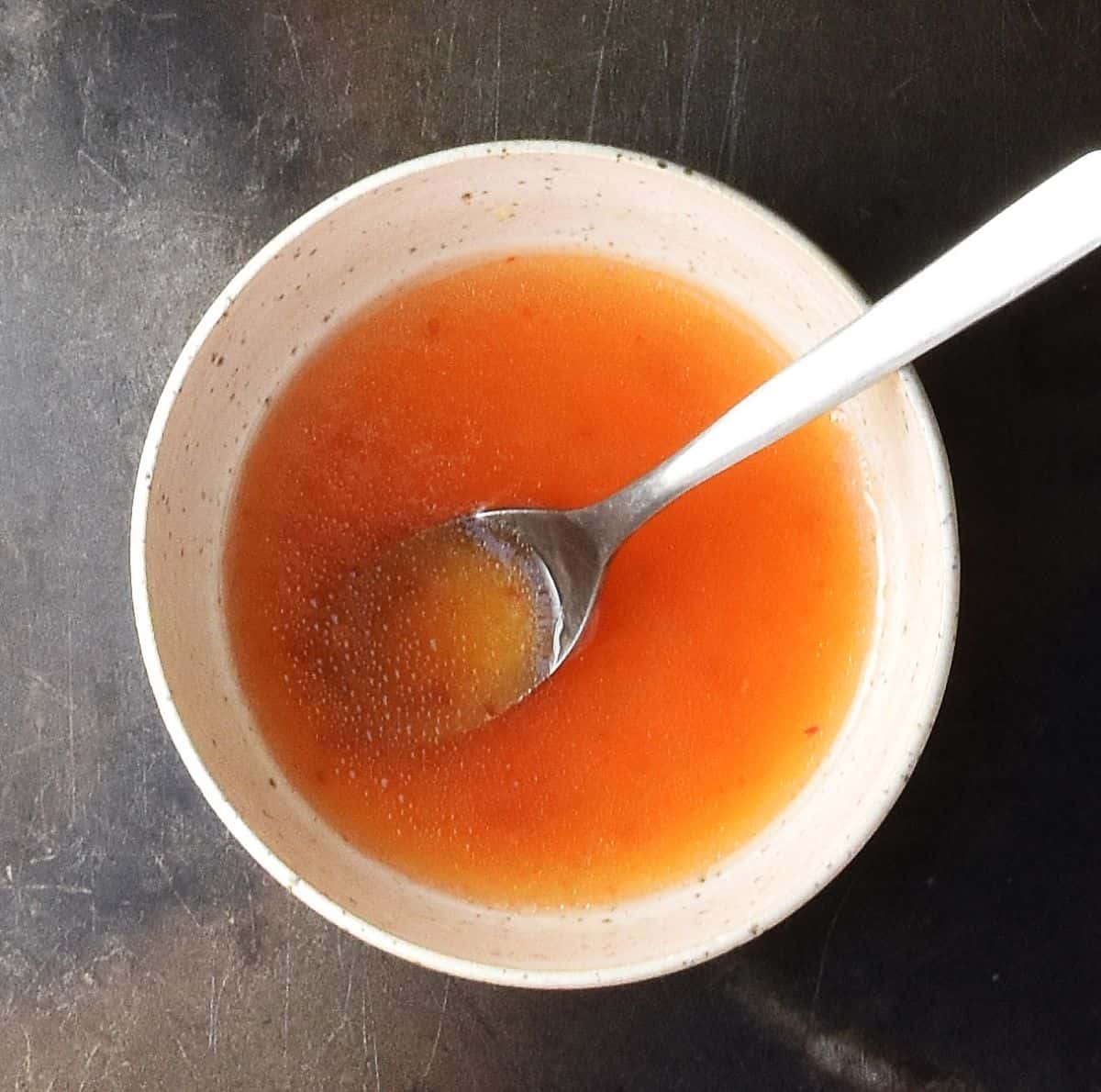 Top down view of sweet chili dressing in white bowl with spoon.