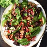 Top down view of beet and chickpea salad with vegetables on white oval plate.