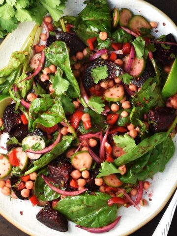 Top down view of beet and chickpea salad with vegetables on white oval plate.