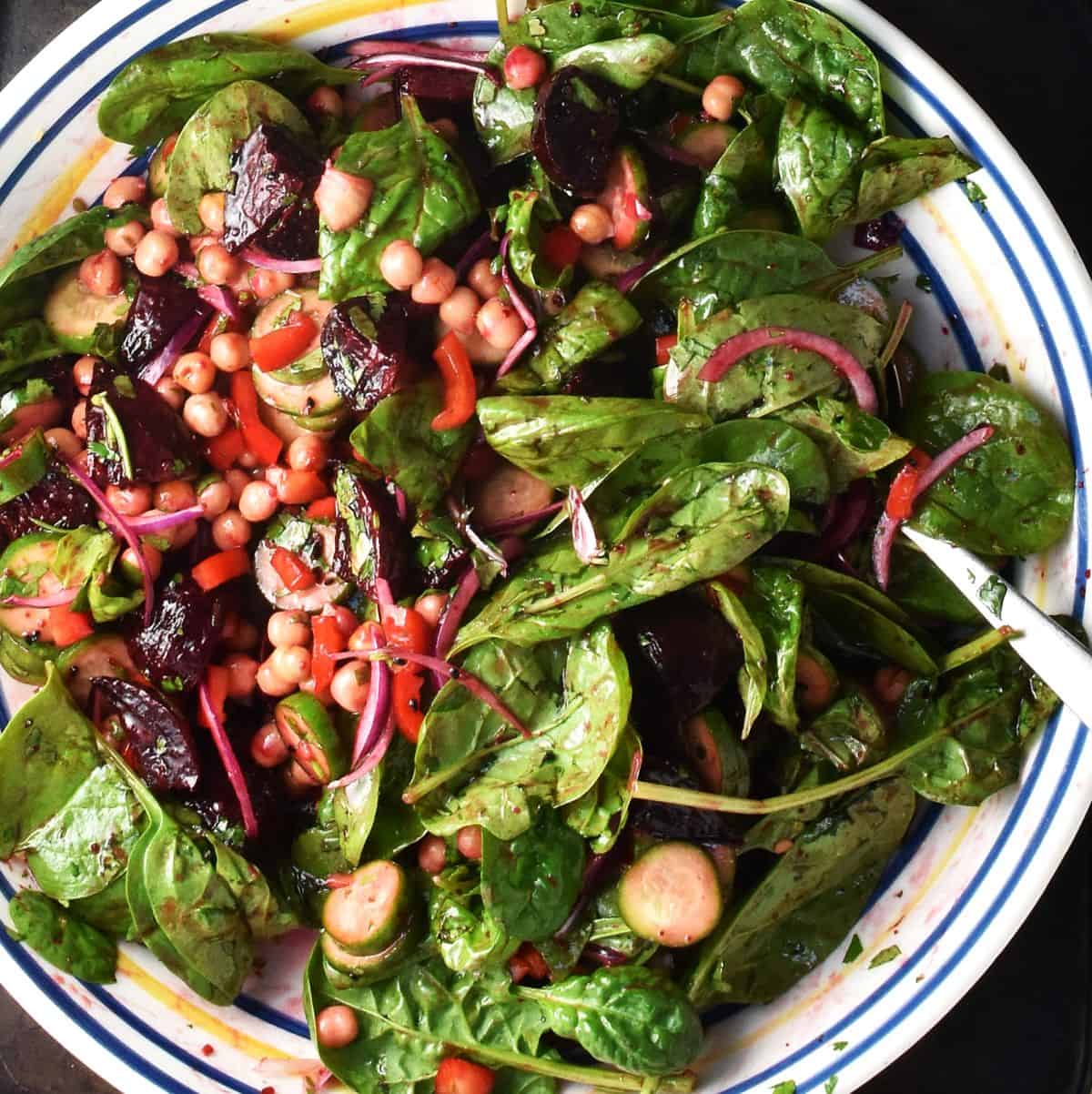 Close-up view of chickpea beet salad with salad greens in large shallow bowl with spoon.