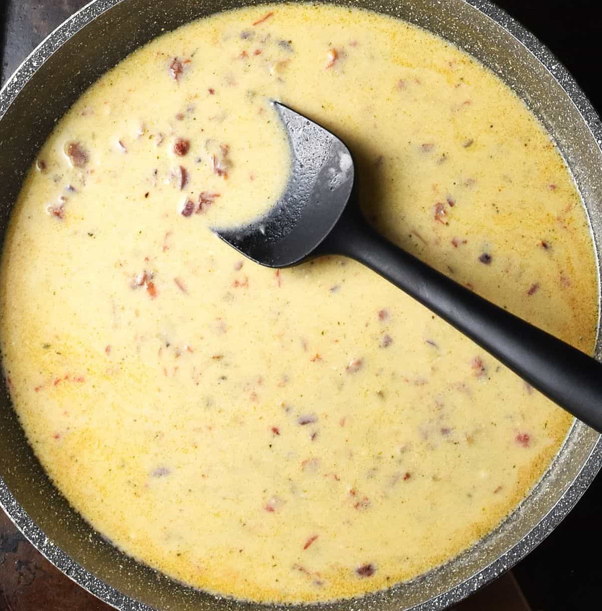 Creamy sun-dried tomato sauce in large speckled pan with black spatula.