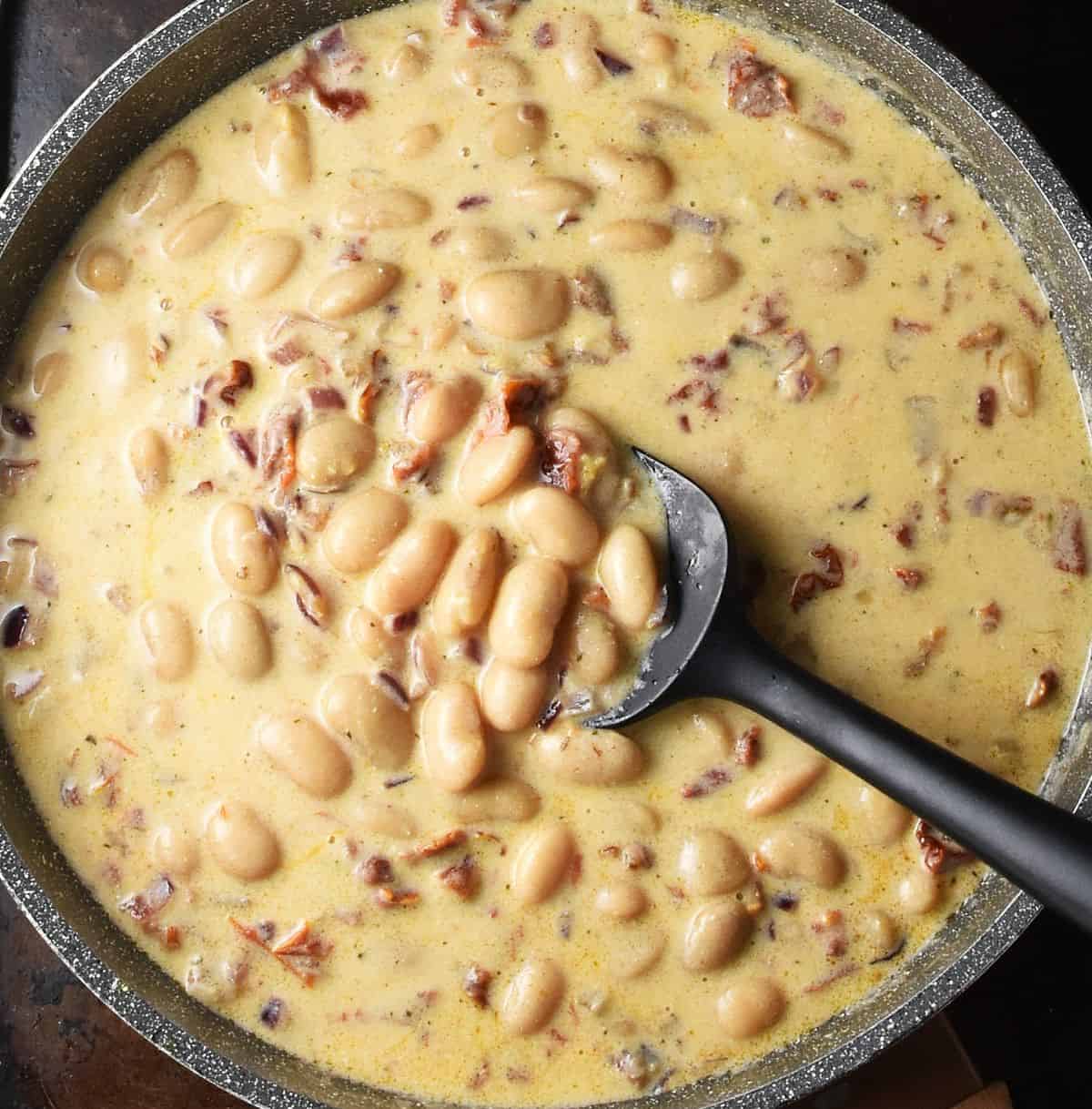Top down view of white beans in sauce in shallow pan.